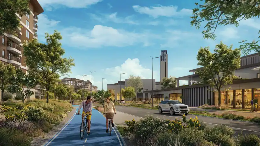 Rendering of a tree-lined street with a blue cycle path where two people ride bicycles, beside a car on the road and a low building with shops.