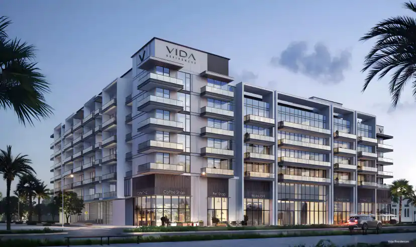 Rendering of a white apartment building seen from a corner at dusk, with stacked balconies, a rooftop sign, ground-floor shopfronts, palm trees, and a parked car.