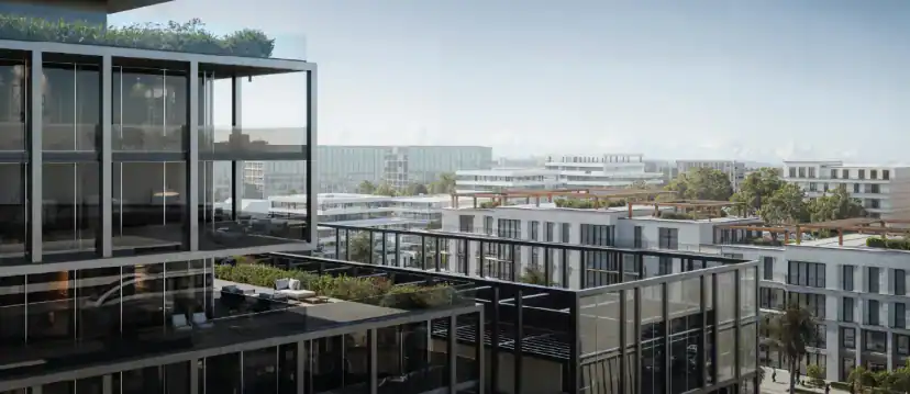 View from a glass-fronted building over terraces with planting toward lower white apartment buildings and a distant skyline under a pale sky.