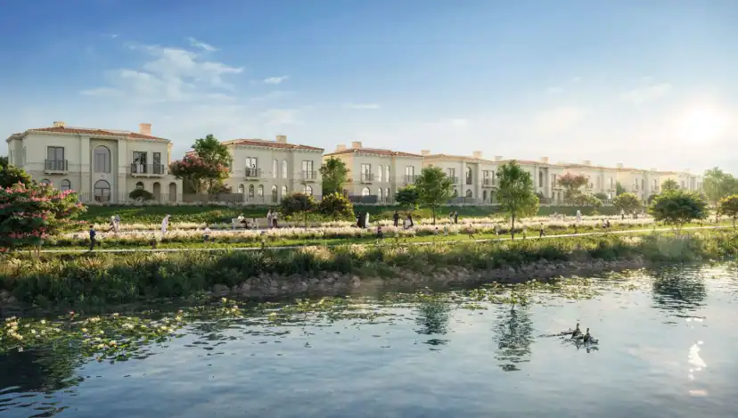 Rendering of a row of cream townhouses with tiled roofs behind a landscaped path with walkers and a calm waterway in the foreground.